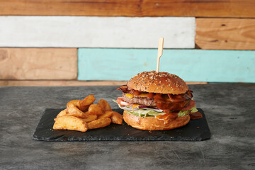 A hamburger with a bun and a piece of potato on a black plate. The bun is brown and the potato is...