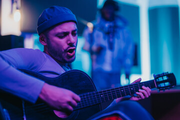 A dedicated musician intensely strumming his guitar in a colorful, atmospheric studio. The creative space is illuminated by dynamic lighting, enhancing the passionate mood of the performance.