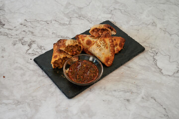 A plate of food with a bowl of sauce next to it. The food is a type of pastry