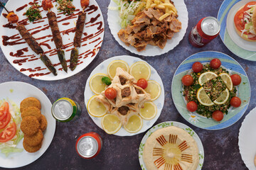 A table with many plates of food and drinks. There are many different types of food, including a variety of meats, vegetables, and desserts. There are also several drinks, including soda and juice