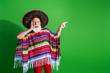 Charismatic old man in traditional Mexican attire posing enthusiastically against a green background