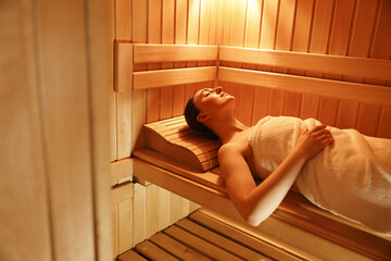 Beautiful woman relaxing on bench in sauna. Space for text