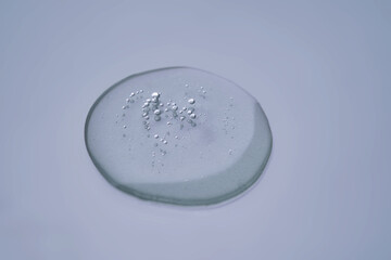 Textured round drop of serum with bubbles on dark blue background.
