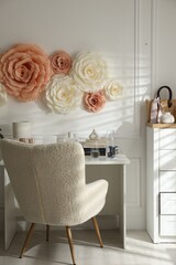 Beautiful decorative paper flowers on white wall and stylish furniture indoors