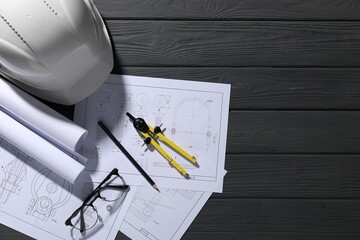 Different engineering drawings, hard hat, glasses, pencil and divider on grey wooden table, flat...
