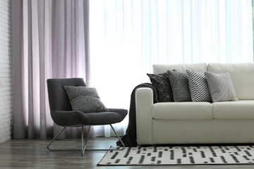 Comfortable sofa and chair near window with elegant curtains in room