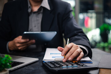 Businessman accountant reviewing financial documents and using a tablet and calculator to plan...