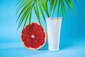 A grapefruit slice and a skincare cream tube are artfully arranged with palm leaves on a vibrant blue background, creating a fresh and tropical aesthetic.