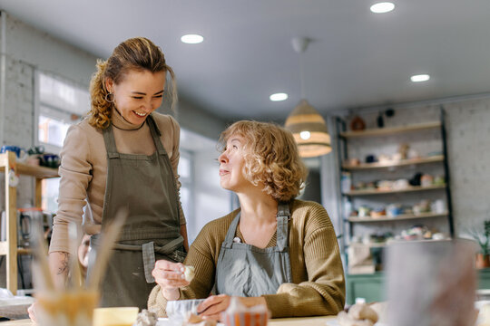 Female artist teaches an elderly woman how to shape clay at a hands-on master class. Happy retired student learns new skills, creating a handmade ceramic bowl