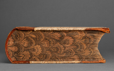 An antique book displayed against a neutral background, showcasing its rich wear and tear. The book's aged pages and cover highlight its historical significance and charm.