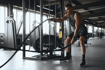 Powerful and muscular man in athletic wear engaging with battle ropes for a workout at the gym....