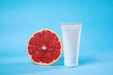 A fresh grapefruit half sits next to a white skincare tube against a vibrant blue backdrop, creating a health-focused and refreshing visual theme.