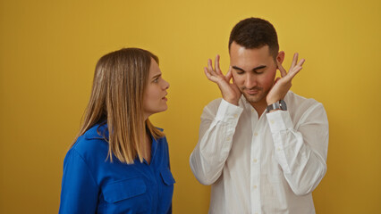 Woman arguing while man covers ears against yellow background, showing frustration in couple's...