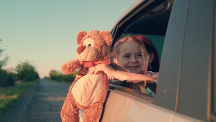 little girl with toy bear. happy face child daughter from window with teddy bear. happy family. mother daughter traveling car. happy mother child back seat car going trip. face childish smile.