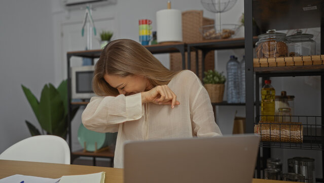Blonde woman sneezing in modern office surrounded by indoor plants and shelves, creating a casual workspace atmosphere.