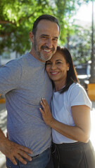 Obraz premium Middle aged hispanic couple smiling warmly in a sunlit urban park represents love and family connection outdoors in a vibrant city setting.