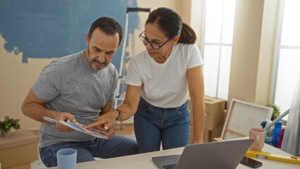 Middle-aged hispanic couple indoors reviewing paint swatches together in their new home living...