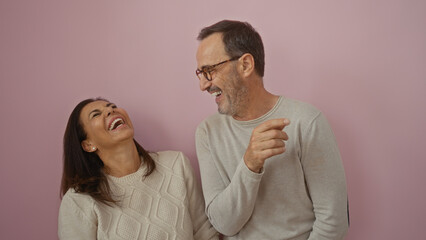 Middle age hispanic man and woman laughing together joyfully against an isolated pink background, expressing love and family connection.
