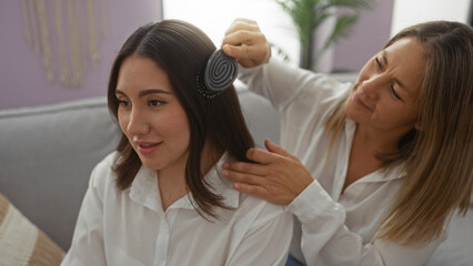 Fototapeta premium Mother brushing daughter's hair in living room showing love and family connection in a cozy home interior, highlighting their bond and care within an apartment setting.