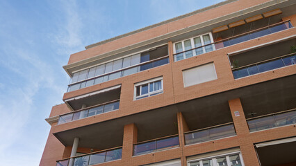 Modern apartment building with glass balconies and brick facade against blue sky in urban...