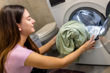 Woman puts bedding in the washing machine.