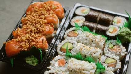 Closeup of sushi rolls with salmon avocado and crunchy topping in plastic takeaway containers for a delicious japanese meal