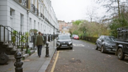 Blurred man walking down a street in chelsea, london with cars parked and trees lining the road during winter.