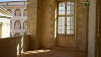Fototapeta premium Defocused view of a historic university campus corridor with sunlight streaming through aged stone architecture and windows, evoking a peaceful and scholarly atmosphere.