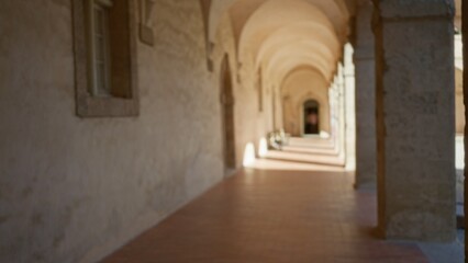 Blurred corridor on university campus features historical architecture with a bokeh effect, emphasizing arches, warm tones, and an inviting sunny atmosphere.