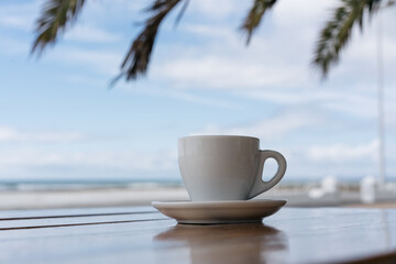 Cup of coffee on a table in a street cafe overlooking the sea and palm trees