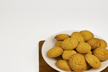 A plate of cookies sits on a wooden board. The cookies are golden brown and appear to be homemade. Concept of warmth and comfort, as the cookies are a popular treat for sharing with friends and family