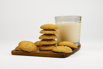 A stack of cookies sits on a wooden board next to a glass of milk. The cookies are arranged in a pyramid shape, with the top cookie being the largest. Concept of comfort and indulgence