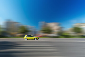 Yellow car is driving down the street. Side view of a fast-moving car against a blurred city background