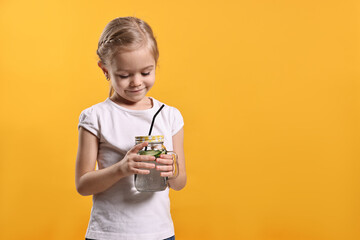Girl with mason jar of cucumber water on orange background, space for text. Refreshing drink