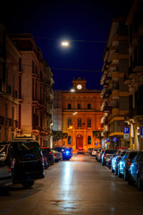 Bari city night street with illuminated streetlights and car lights reflected on the rainy road in Puglia (Apulia), Italy&mdash;capturing the glow of urban life after rain.