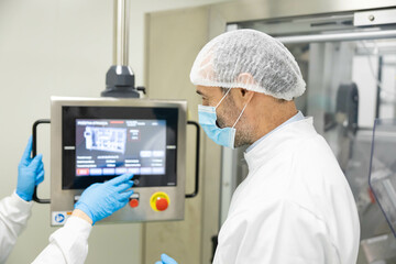 Two professionals converse about machinery settings against a backdrop of cleanroom standards, showcasing their teamwork and expertise.