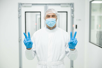 A healthcare worker dressed in protective gear displays peace signs in a cleanroom, emphasizing...