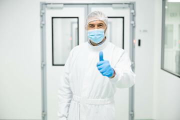 A healthcare professional in cleanroom attire gives a thumbs up gesture, signifying confidence and...