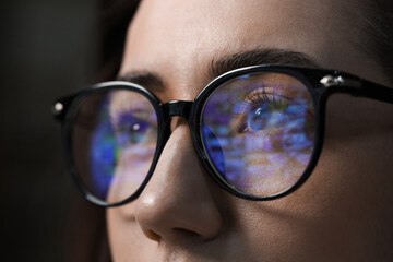 Young woman wearing glasses with reflection on dark background, closeup