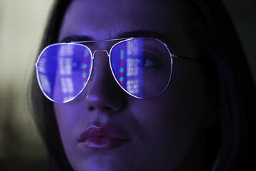 Young woman wearing glasses with reflection on dark background, closeup