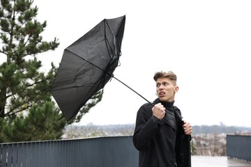 Man with broken umbrella fighting wind under rain outdoors