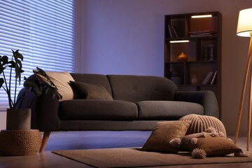 Stylish living room with comfortable sofa and wooden shelving unit in evening. Interior design