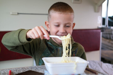 Child eating fast food on train. Little boy eating noodles on train sitting by the window.