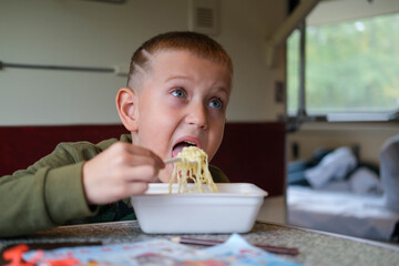 Child eating fast food on train. Little boy eating noodles on train sitting by the window.