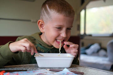 Child eating fast food on train. Little boy eating noodles on train sitting by the window.