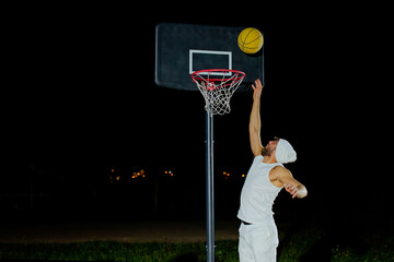 A man performs a slam dunk on a basketball court at night under the glare of bright outdoor lights