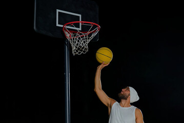 A man performs a slam dunk on a basketball court at night under the glare of bright outdoor lights