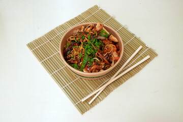 A bowl of food with chopsticks on a bamboo mat. The food is a mix of noodles and meat
