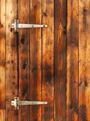 Fragment of natural yellow wooden door with brown stains, showcasing the texture and grain of the wood. Large metal hinges
