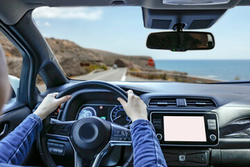 Naklejka premium Woman's hands on steering wheel in car. Through car windshield visible landscape of road in mountains along the seashore.
